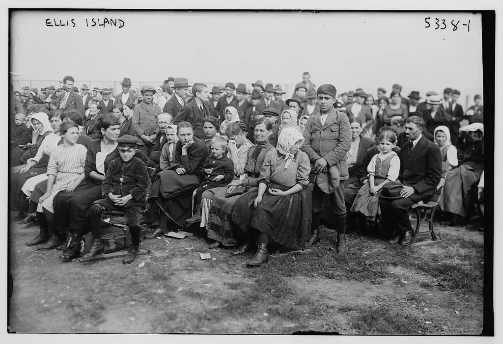 Black and white photograph of immigrants waiting at Ellis Island, representing the experience of European immigrants arriving in America whose names were often anglicized or changed in official records during the immigration process.