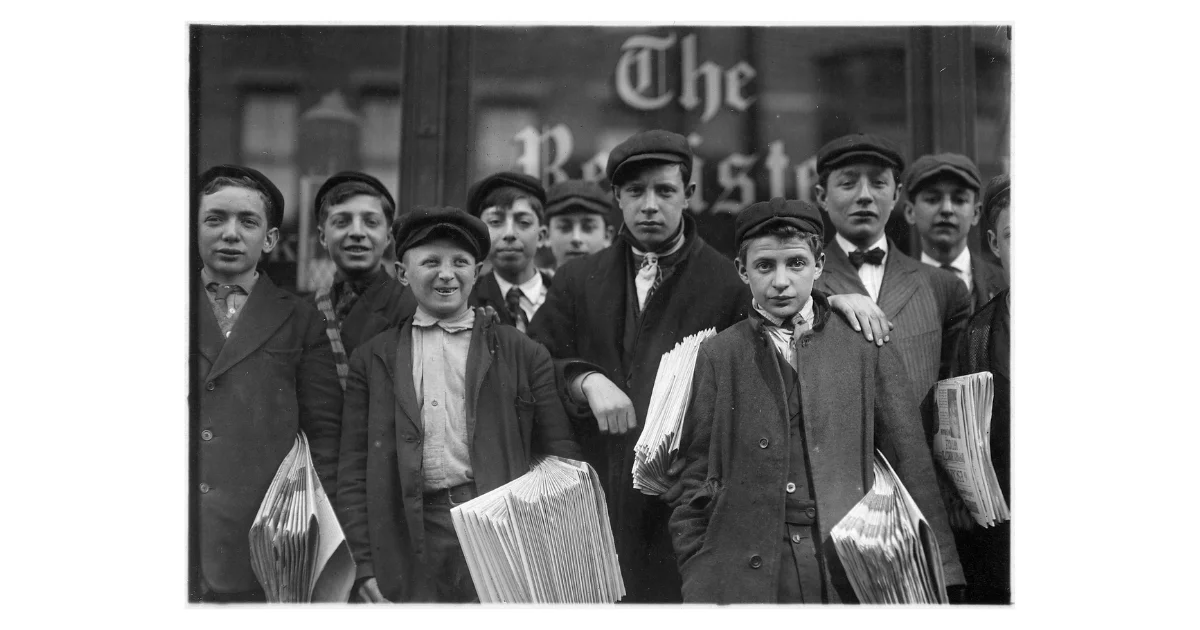 Black and white photograph of a group of young newsboys holding stacks of newspapers, standing in front of a building with "The Register" visible in the window behind them, New Haven, Connecticut, early 1900s.