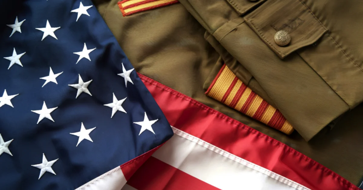 An American flag draped alongside a folded olive military uniform with gold service stripes and brass buttons, representing veterans of the United States armed forces across multiple conflicts.